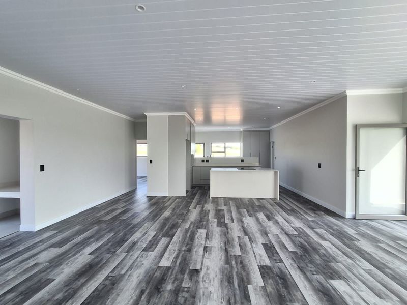 Spacious open-plan living and kitchen area featuring modern laminate flooring, a central kitchen island, and a clean, neutral aesthetic with recessed lighting.