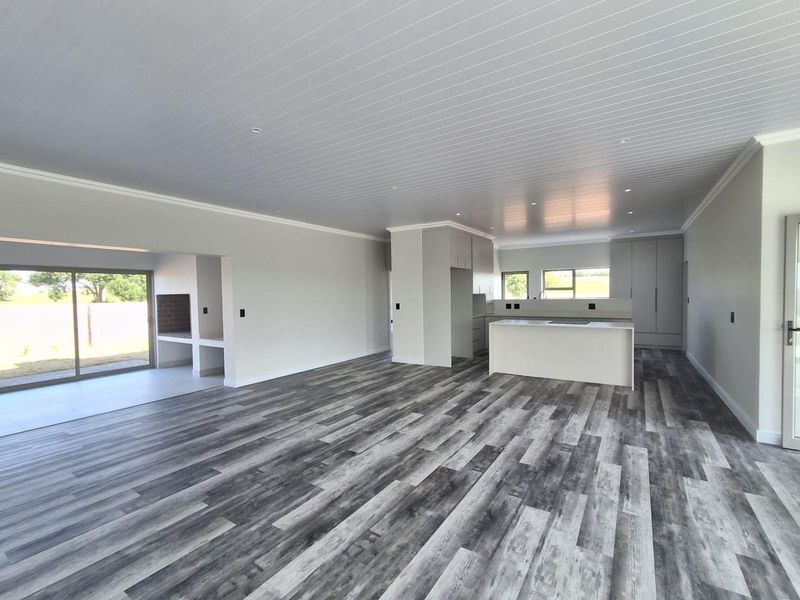 Spacious open-plan living area featuring modern kitchen cabinetry, a central island, laminate flooring, and a built-in indoor braai area with sliding door access.