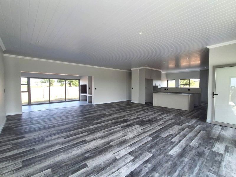 Spacious open-plan living area featuring modern laminate flooring, a sleek kitchen with island, and large sliding doors leading to an outdoor patio space.