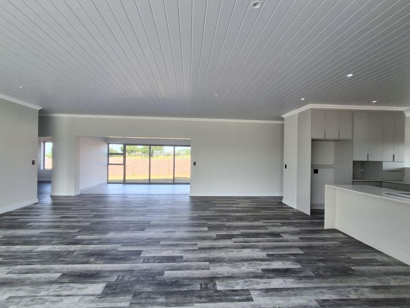 Spacious open-plan living area featuring modern laminate flooring, a tongue and groove ceiling with recessed lighting, and a sleek kitchen with island.