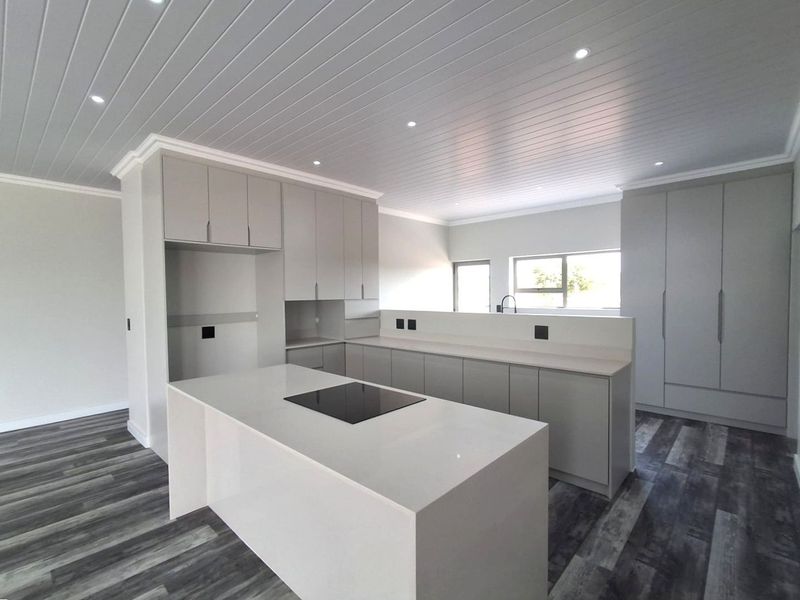Modern, newly renovated kitchen featuring a central island with induction hob, sleek cabinetry, stone countertops, and contemporary tongue and groove ceiling finishes.
