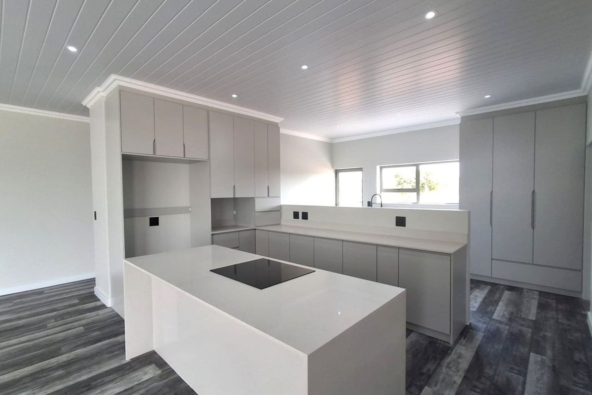 Modern, newly renovated kitchen featuring a central island with induction hob, sleek cabinetry, stone countertops, and contemporary tongue and groove ceiling finishes.