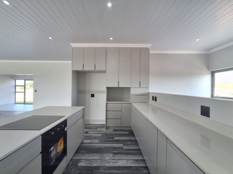 Modern kitchen featuring sleek grey cabinetry, stone countertops, integrated oven, electric cooktop, and recessed lighting with a clean, contemporary aesthetic.