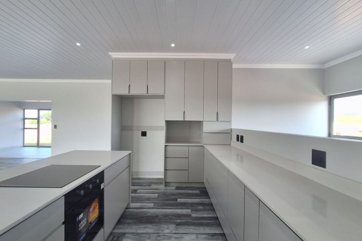 Modern kitchen featuring sleek grey cabinetry, stone countertops, integrated oven, electric cooktop, and recessed lighting with a clean, contemporary aesthetic.