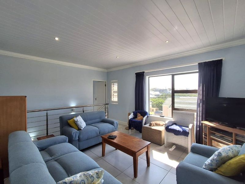 A bright living room featuring tiled floors, a tongue and groove ceiling with recessed lighting, and a stainless steel balustrade overlooking the lower level.