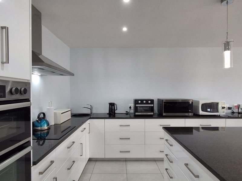 Modern kitchen featuring white cabinetry, black granite countertops, a central island, built-in oven, and sleek pendant lighting.