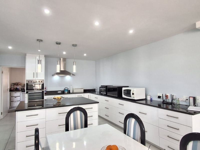 Modern kitchen featuring a central island, granite countertops, built-in oven, extractor fan, and ample white cabinetry with recessed lighting.