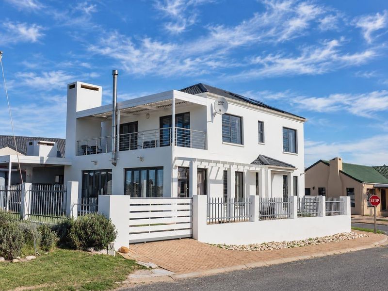 A modern two-story residential property featuring a white facade, upper-level balcony with metal balustrades, external chimney, and a secure gated entrance with paved driveway.