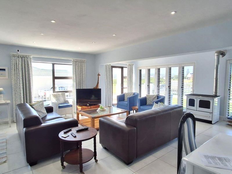 Spacious living room featuring tiled flooring, recessed lighting, and a freestanding wood-burning stove, with large windows and sliding doors providing ample natural light.