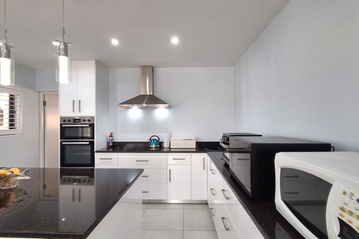 Modern kitchen featuring white cabinetry, granite countertops, a central island, and built-in double oven with stainless steel extractor fan.