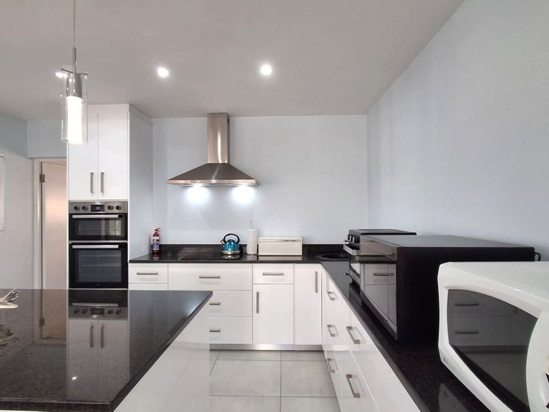 Modern kitchen featuring white cabinetry, granite countertops, a central island, and built-in double oven with stainless steel extractor fan.