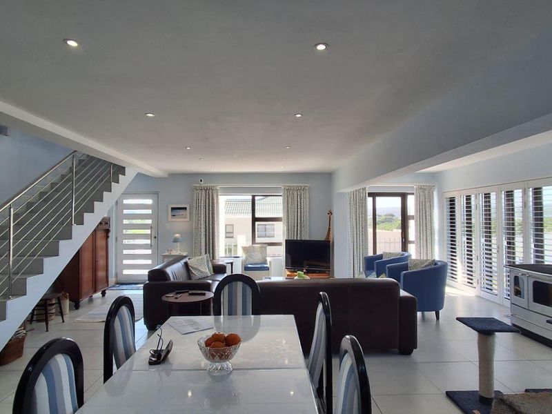 Spacious open-plan living and dining area featuring tiled floors, a modern staircase with stainless steel balustrades, and a built-in wood-burning stove.