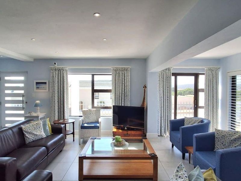 Spacious living room featuring tiled flooring, recessed downlights, and large windows with shutters, providing ample natural light and access to the outdoor area.