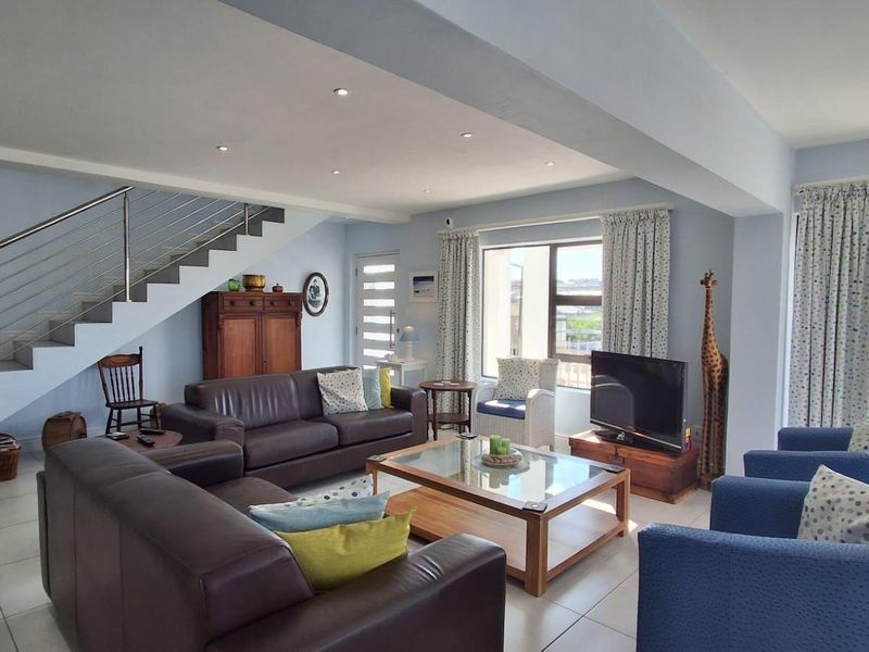 Spacious open-plan living area featuring a modern staircase with stainless steel balustrades, tiled flooring, and large windows providing ample natural light.