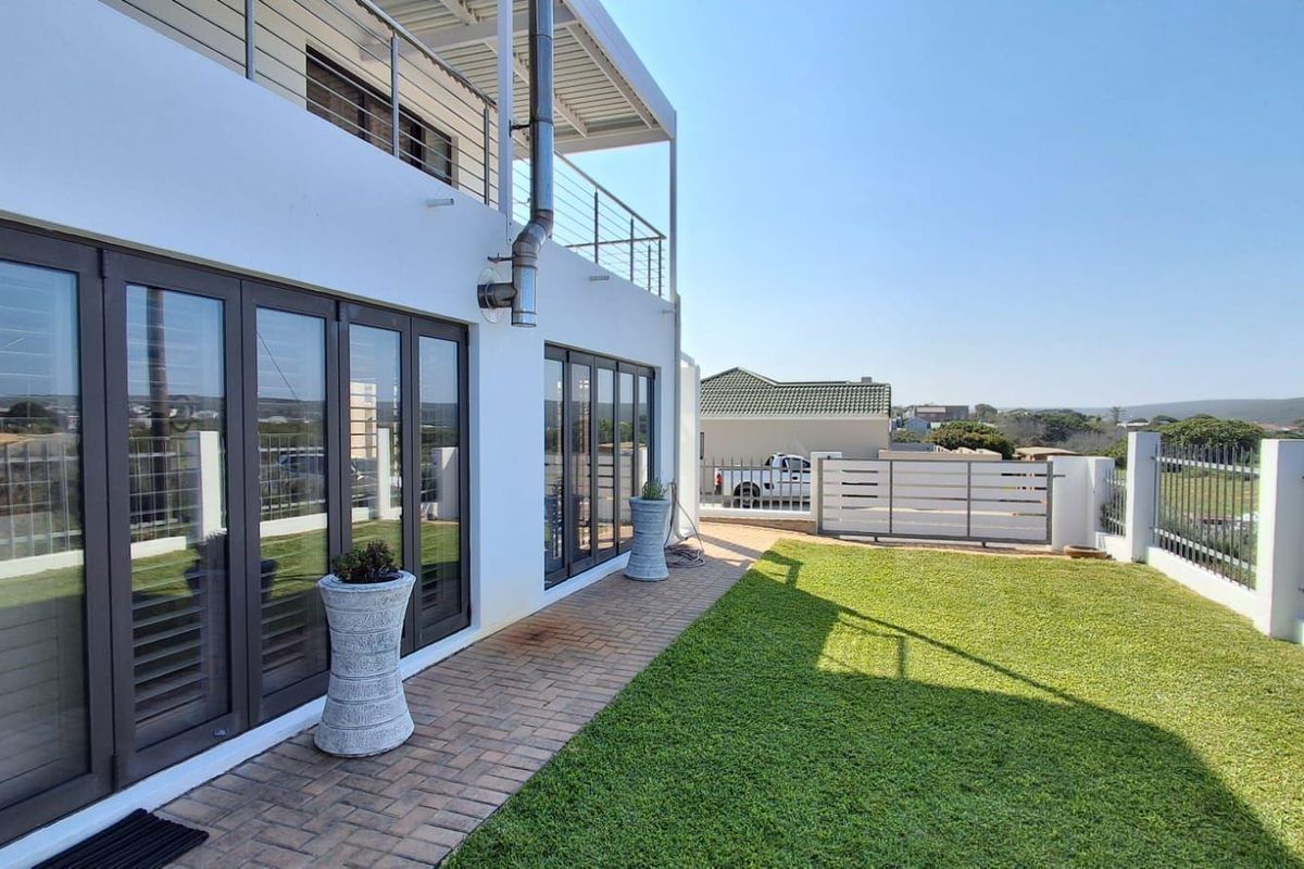 A well-maintained rear exterior featuring a paved patio, manicured lawn, secure perimeter fencing, and bi-fold doors leading to the main living area.