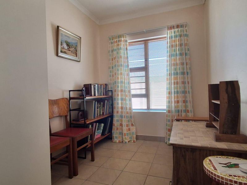 A compact bedroom featuring tiled flooring, a built-in cupboard, and a window with horizontal blinds, offering a functional and neutral living space.