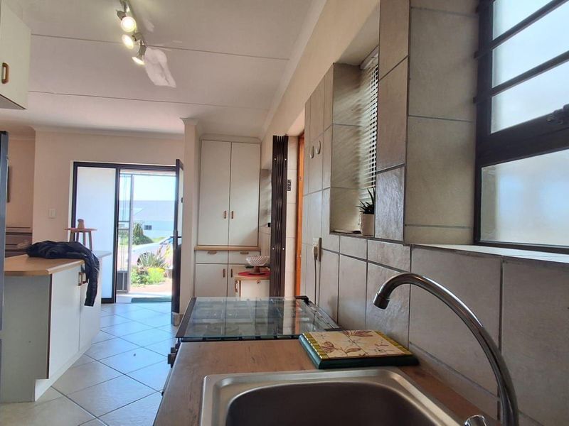 A functional kitchen featuring tiled finishes, built-in cabinetry, a stainless steel sink, and a hob, with direct access to an outdoor area.