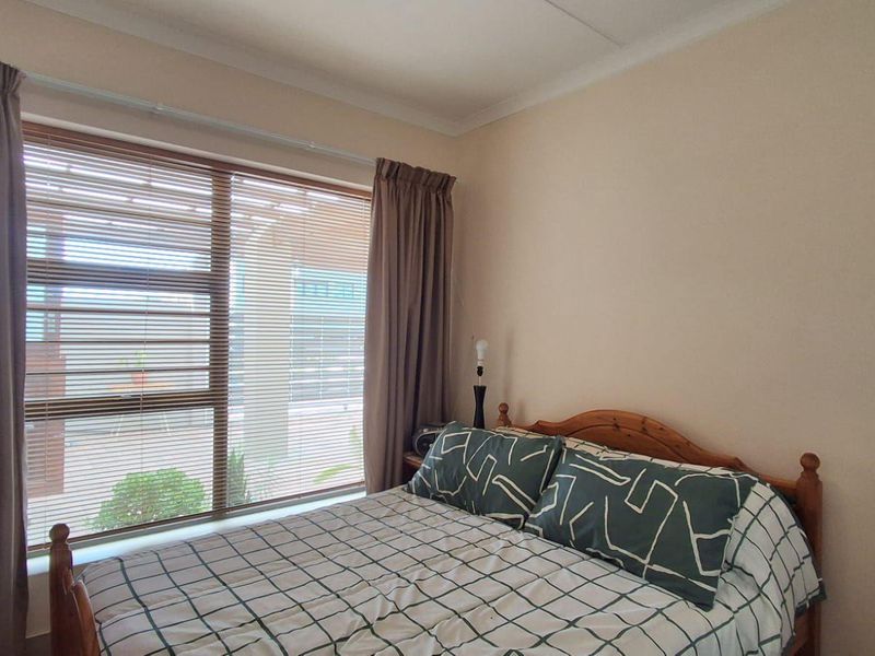 A standard bedroom featuring a large window with venetian blinds and neutral wall finishes, providing a functional and well-lit sleeping space.