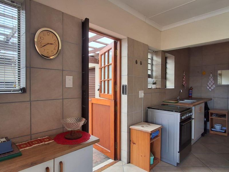 A functional kitchen featuring tiled walls and flooring, built-in cabinetry, a stainless steel sink, and a freestanding stove with direct access to an outdoor area.