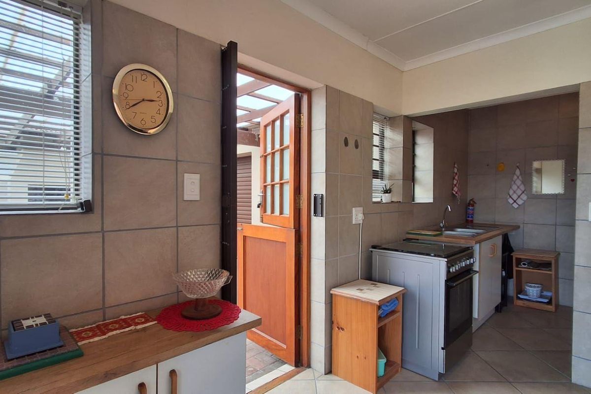 A functional kitchen featuring tiled walls and flooring, built-in cabinetry, a stainless steel sink, and a freestanding stove with direct access to an outdoor area.