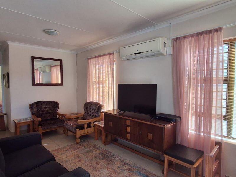 A comfortable living room featuring tiled flooring, a wall-mounted air conditioning unit, and large windows that provide natural light.