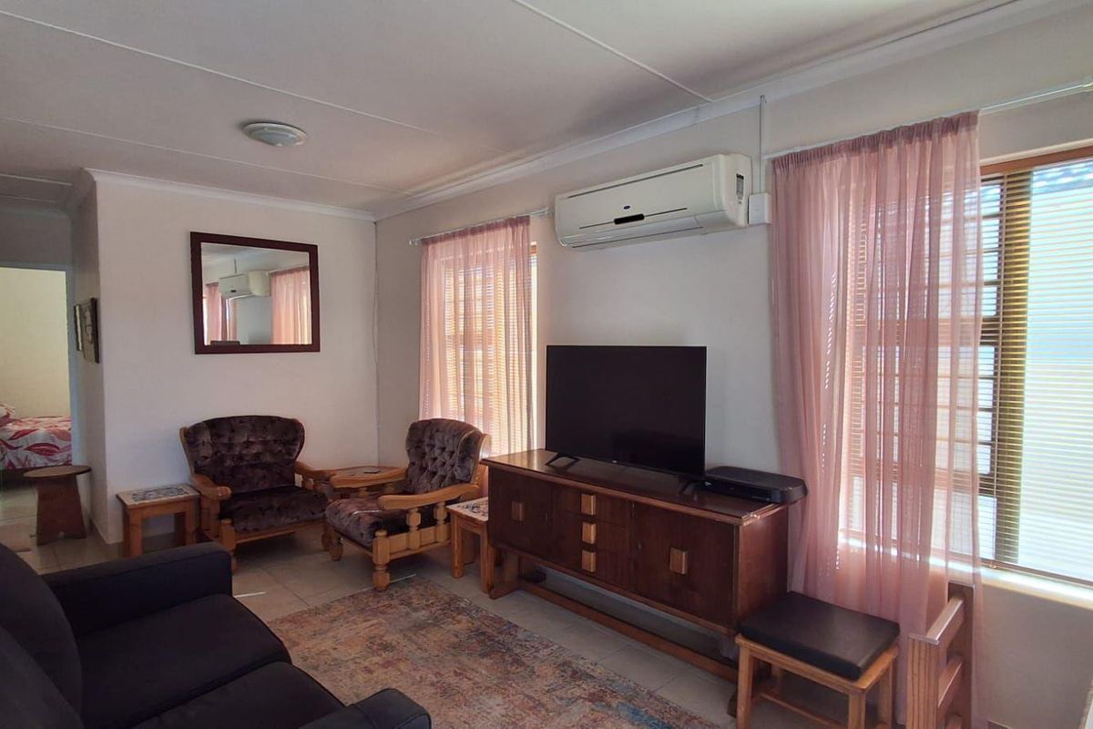 A comfortable living room featuring tiled flooring, a wall-mounted air conditioning unit, and large windows that provide natural light.