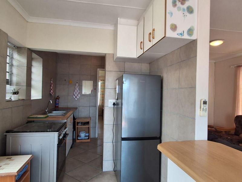 A functional kitchen featuring tiled walls and flooring, built-in cabinetry, a double sink, and a breakfast counter connecting to the adjacent living area.