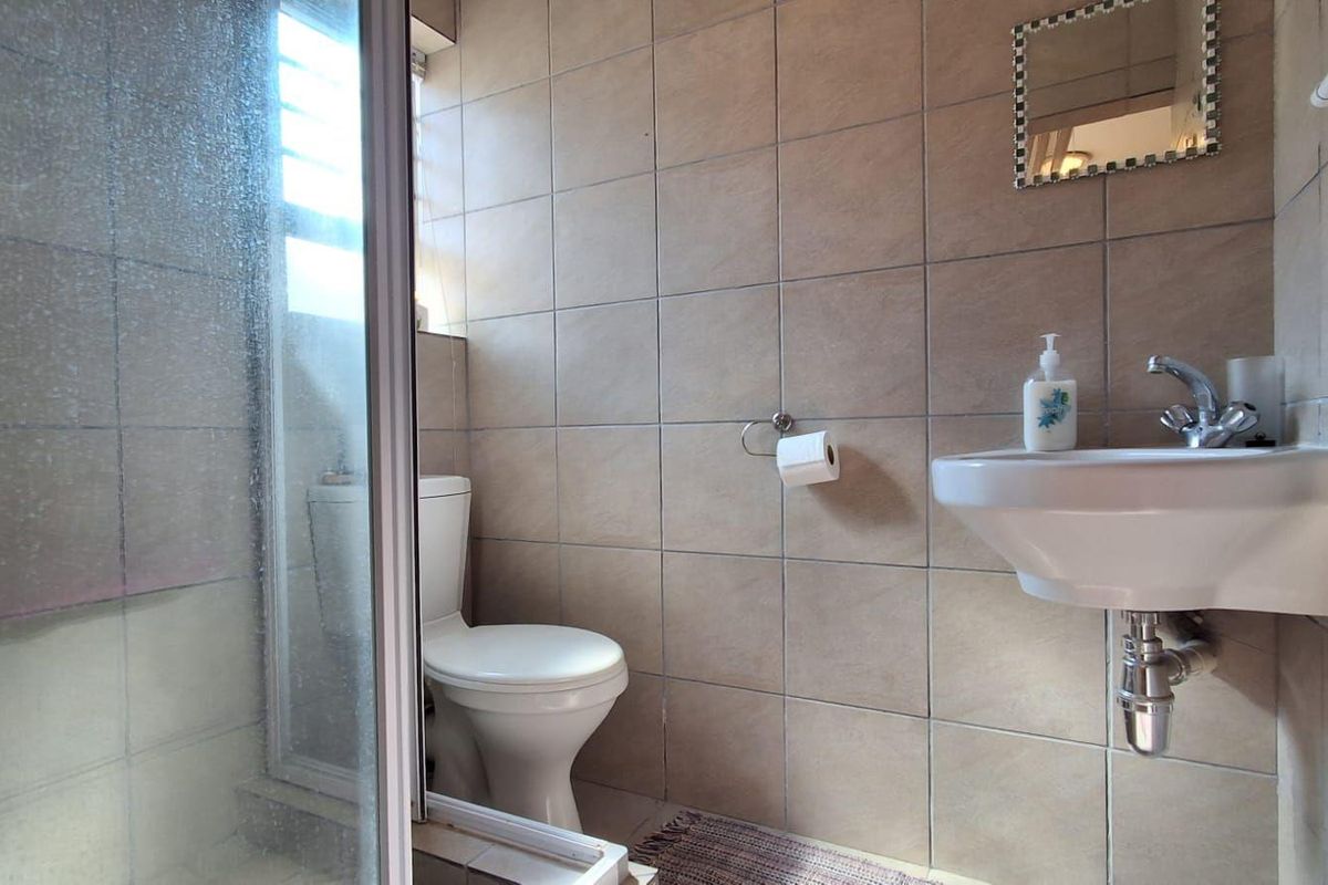 A compact bathroom featuring a shower enclosure, wall-mounted basin, and toilet with neutral wall tiling.