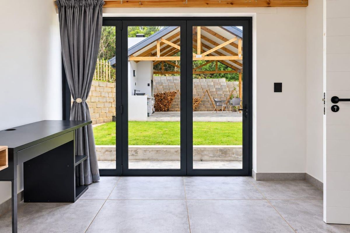 Bright living area featuring large format floor tiles and modern black aluminium bifold doors opening onto a landscaped garden and outdoor entertainment space.