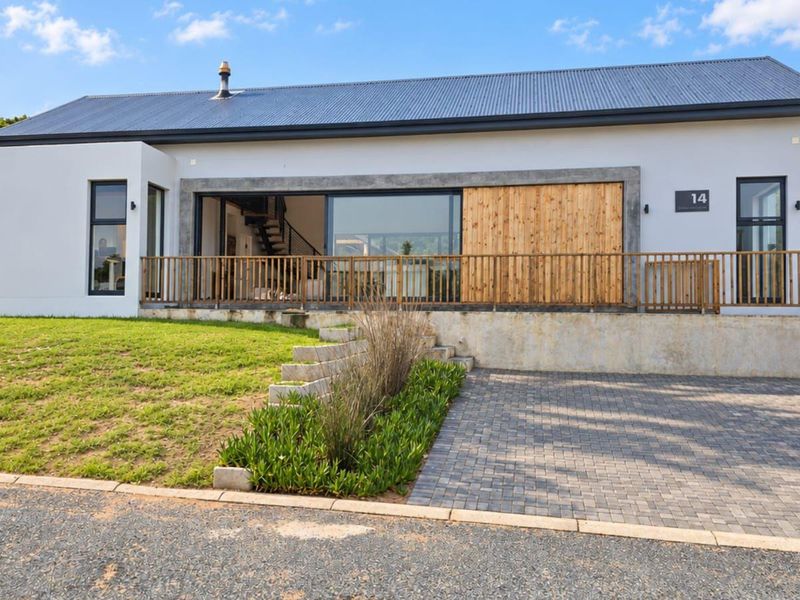 Modern single-story residence featuring a corrugated metal roof, timber accents, large sliding glass doors, and a paved driveway with landscaped garden.