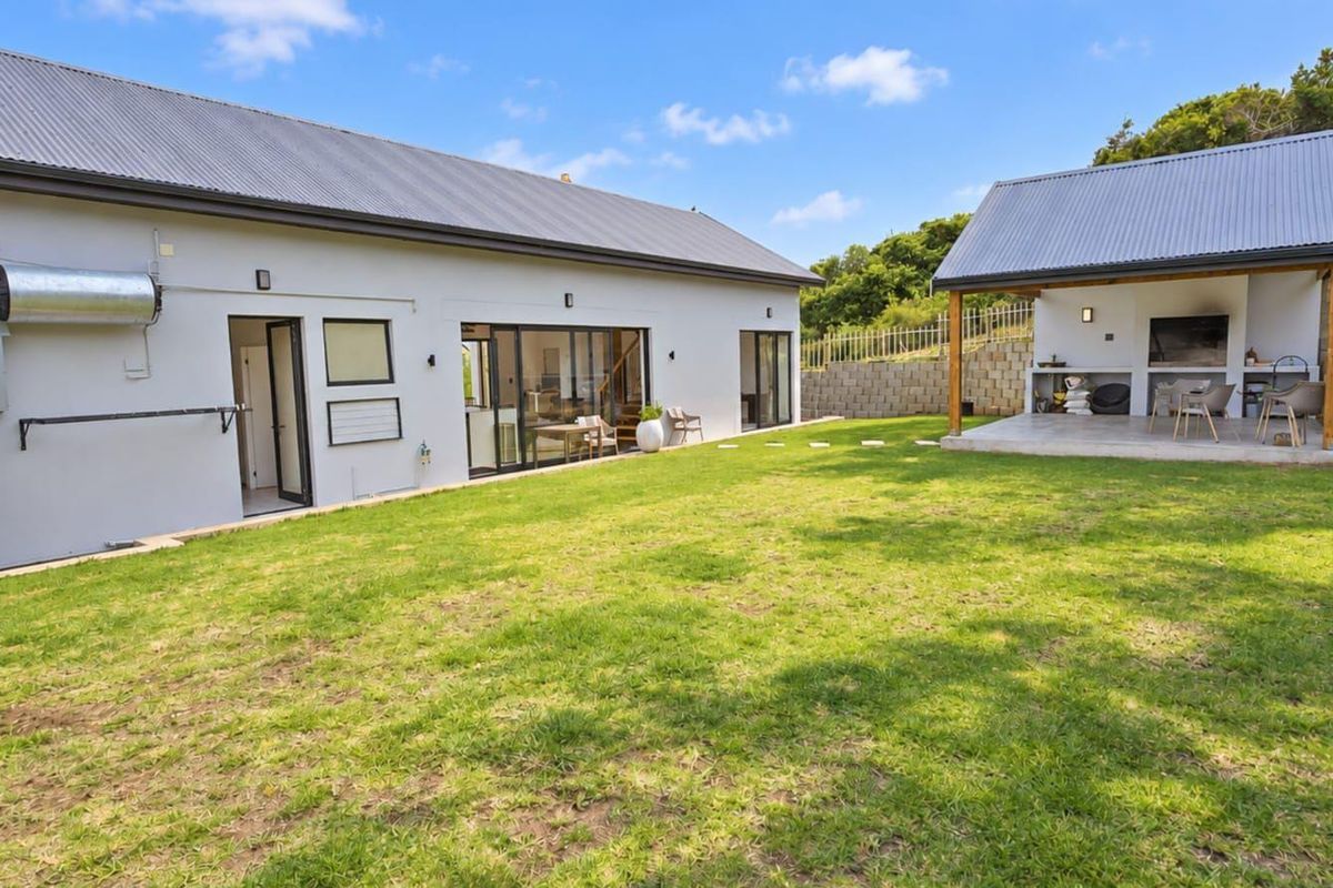 Spacious rear garden featuring a main dwelling with sliding doors, a separate covered patio area with a built-in braai, and a water tank.