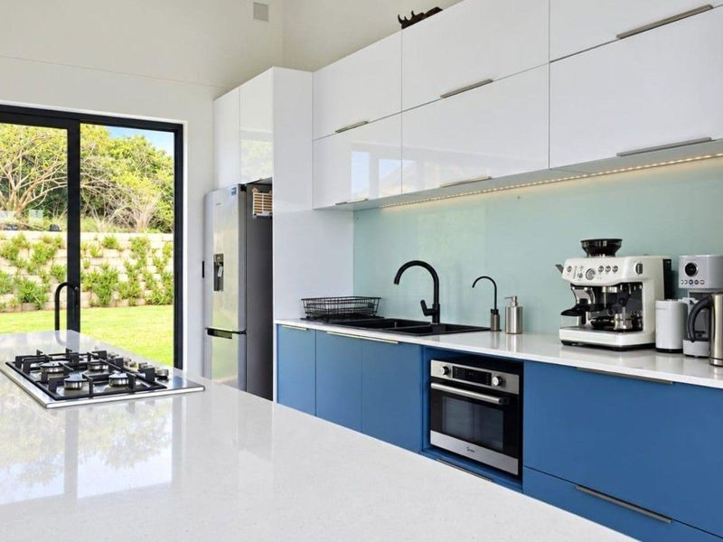 Modern kitchen featuring blue lower cabinetry, white upper cabinets, quartz countertops, integrated gas cooktop, and direct access to the garden through sliding glass doors.