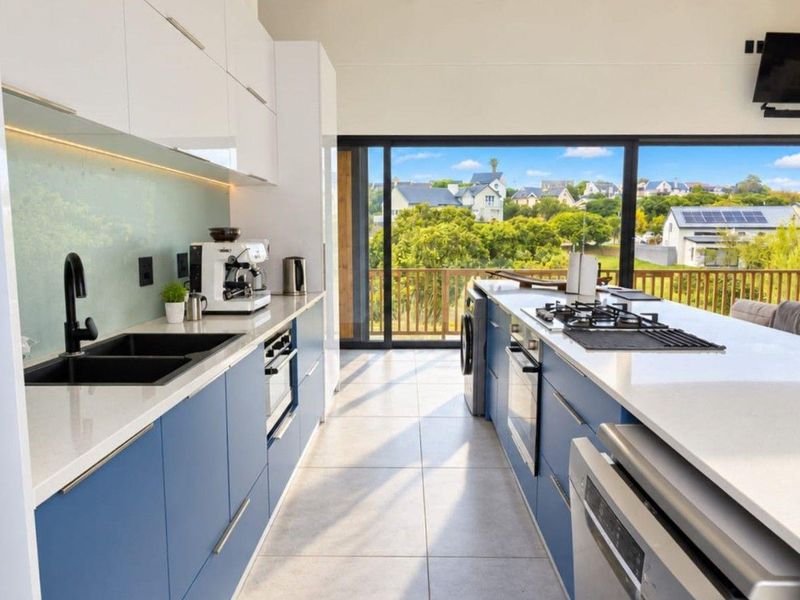 Modern kitchen featuring sleek blue cabinetry, stone countertops, integrated appliances, and large sliding doors opening to a scenic outdoor view.