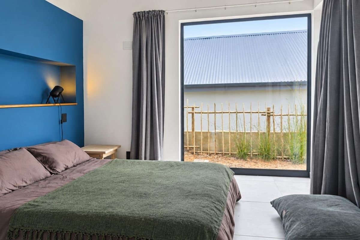 Modern bedroom featuring a bold blue accent wall with a built-in niche and a large window providing natural light and garden views.