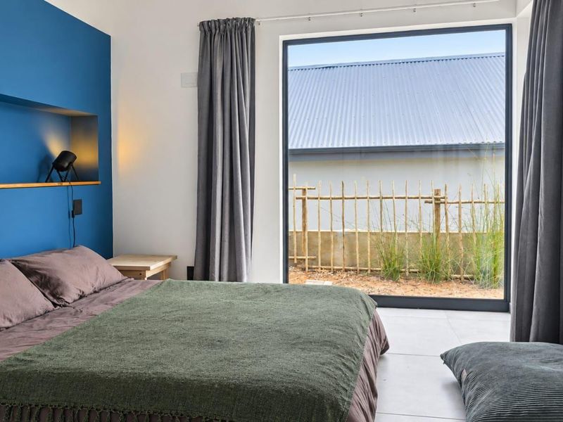 Modern bedroom featuring a bold blue accent wall with a built-in niche and a large window providing natural light and garden views.