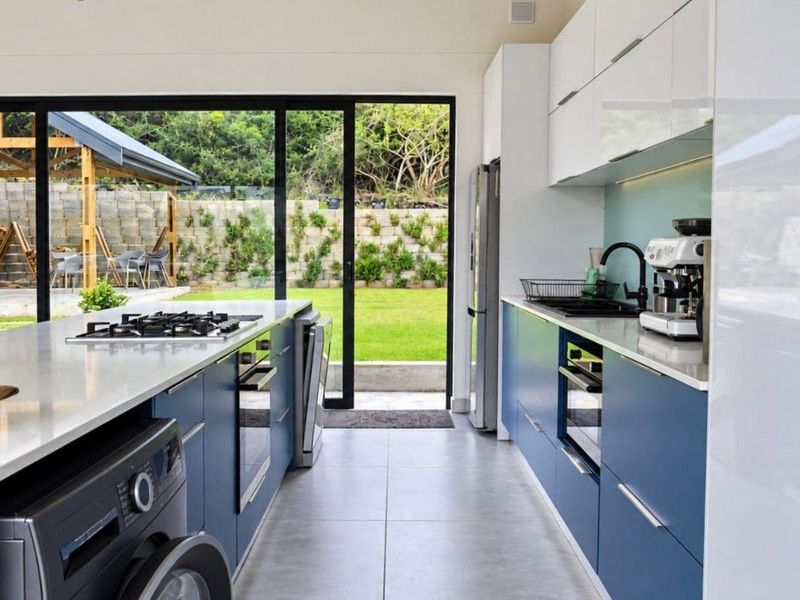 Modern kitchen featuring blue and white cabinetry, stone countertops, gas hob, and large sliding glass doors opening to a landscaped garden.