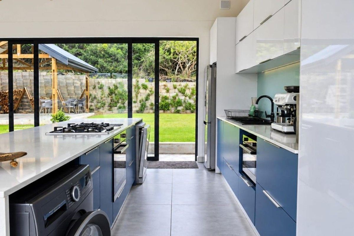Modern kitchen featuring blue and white cabinetry, stone countertops, gas hob, and large sliding glass doors opening to a landscaped garden.