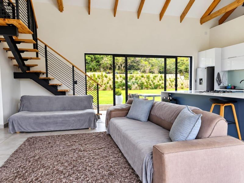 Spacious open-plan living area featuring a modern kitchen with island, exposed timber ceiling beams, and a striking industrial-style staircase leading to the upper level.
