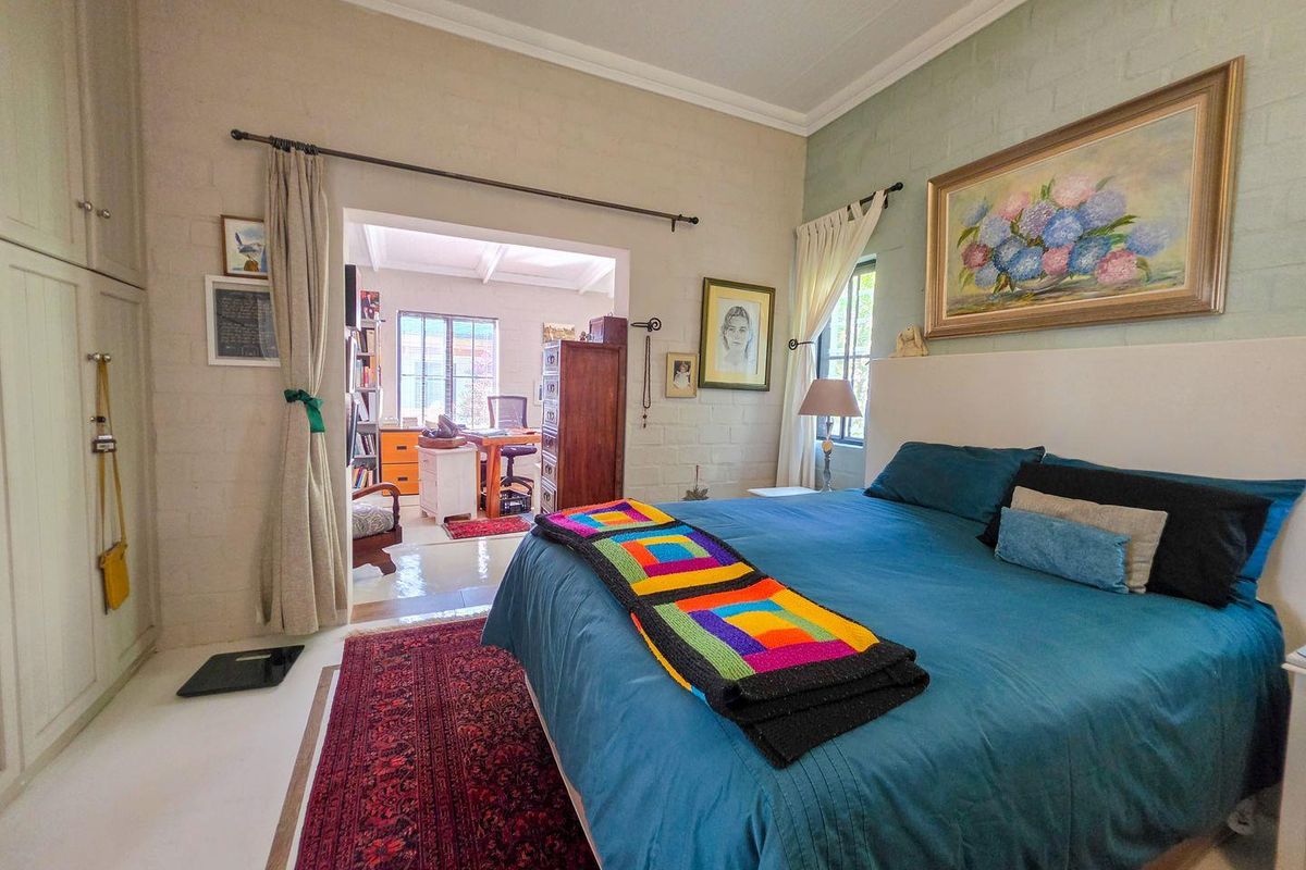 Spacious bedroom featuring built-in cupboards, painted brick walls, and a ceiling fan, with an adjoining study area visible through the doorway.