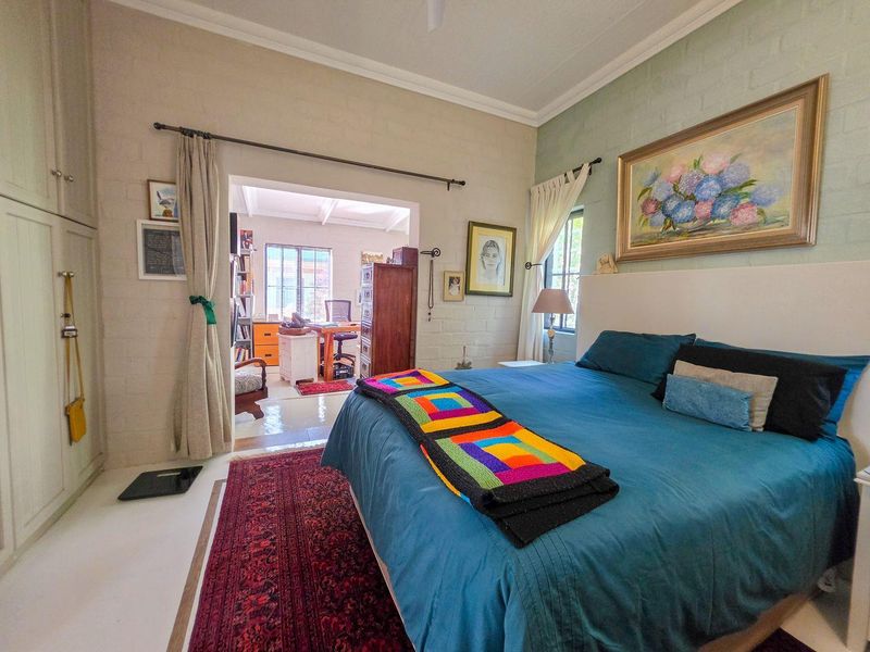 Spacious bedroom featuring built-in cupboards, painted brick walls, and a ceiling fan, with an adjoining study area visible through the doorway.