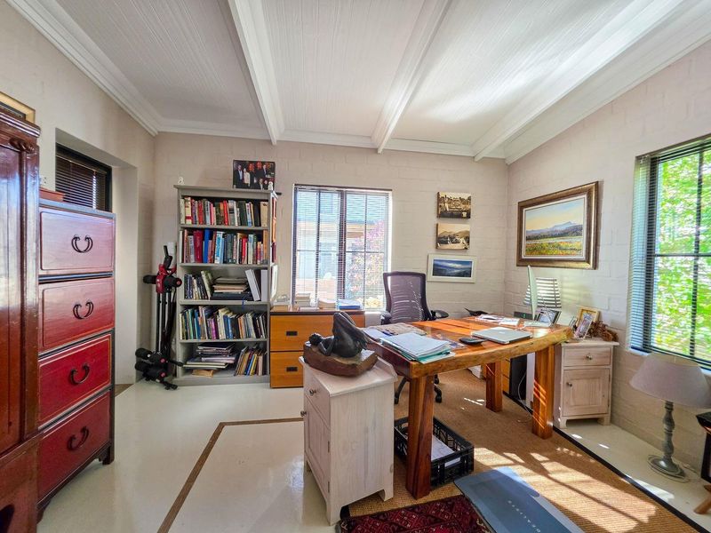 A bright home office featuring painted brick walls, exposed beam ceilings, and natural light through venetian blinds.