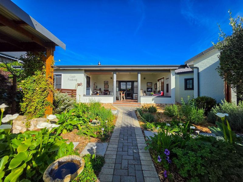 A well-maintained rear exterior view featuring a covered patio, brick paved pathway, and established landscaped garden leading to the main residence.