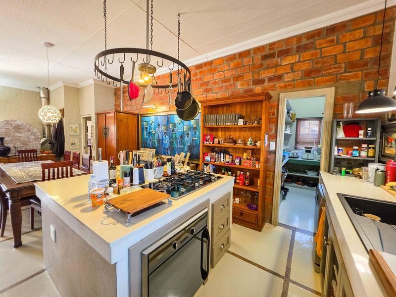 Spacious open-plan kitchen featuring an exposed brick wall, central island with gas hob and oven, and an adjoining scullery area.