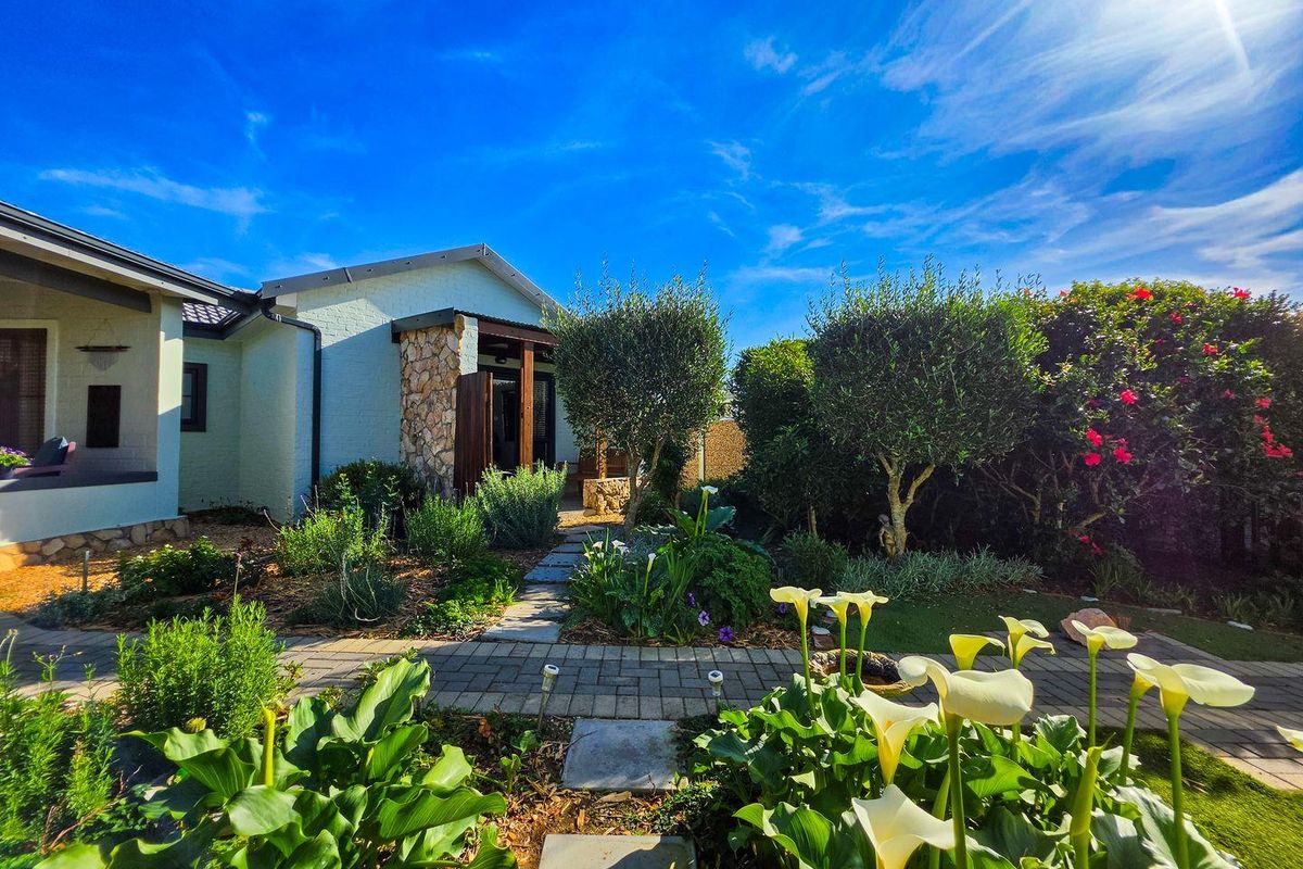 A well-maintained rear garden featuring a stone-clad exterior wall, paved pathways, and established landscaping leading to a covered patio area.