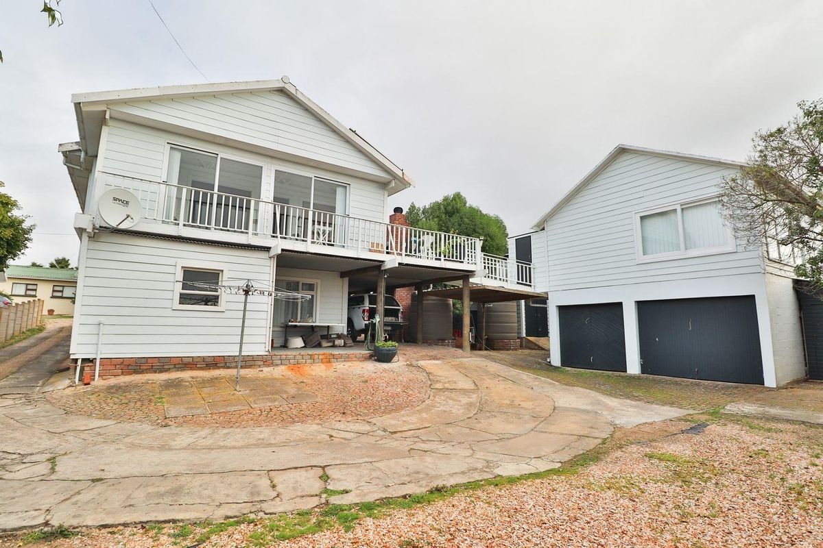 Rear view of the property featuring a raised timber deck, weatherboard cladding, double garage, and a concrete driveway area.
