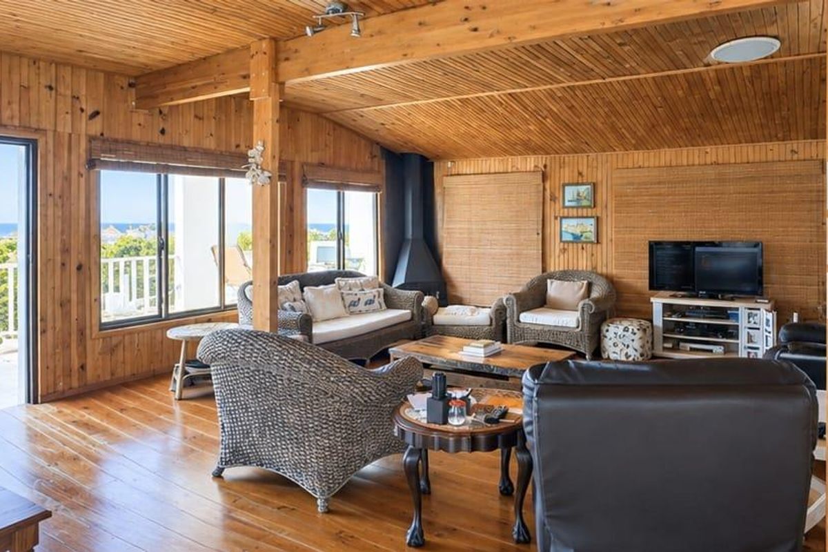 Spacious living room featuring extensive timber wall and ceiling paneling, hardwood floors, a freestanding fireplace, and direct access to an outdoor balcony with views.