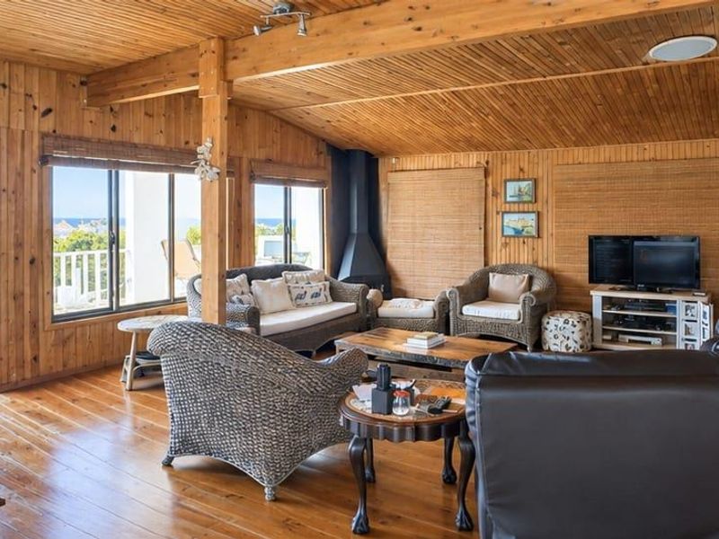 Spacious living room featuring extensive timber wall and ceiling paneling, hardwood floors, a freestanding fireplace, and direct access to an outdoor balcony with views.