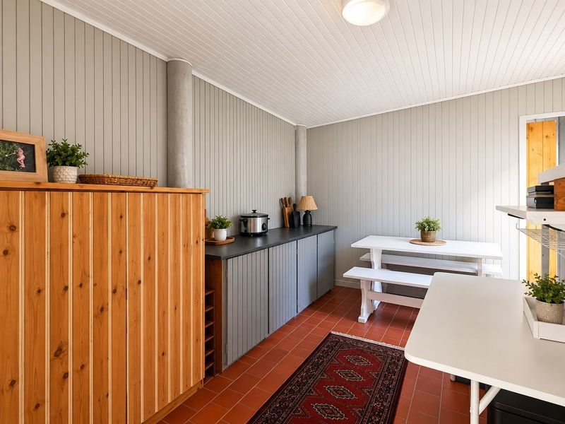A functional scullery or utility area featuring built-in cabinetry, dark countertops, tongue and groove wall paneling, and durable terracotta tile flooring.