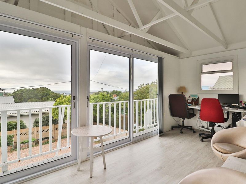 Bright home office featuring vaulted ceilings with exposed rafters, laminate flooring, and large sliding glass doors opening onto a balcony with scenic views.