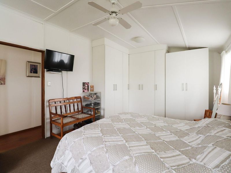 A functional bedroom featuring built-in white wardrobes, a ceiling fan, and neutral carpeting, offering a clean and practical living space.